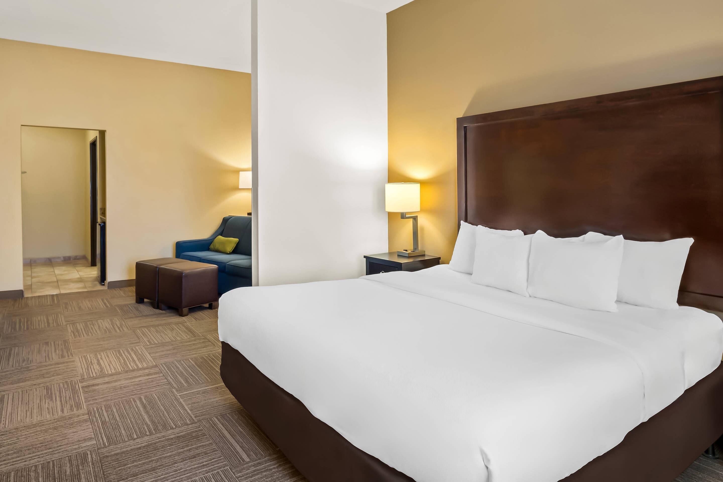 Una camera d'albergo con un letto grande, un comodino con una lampada, una sedia blu e un tavolino.