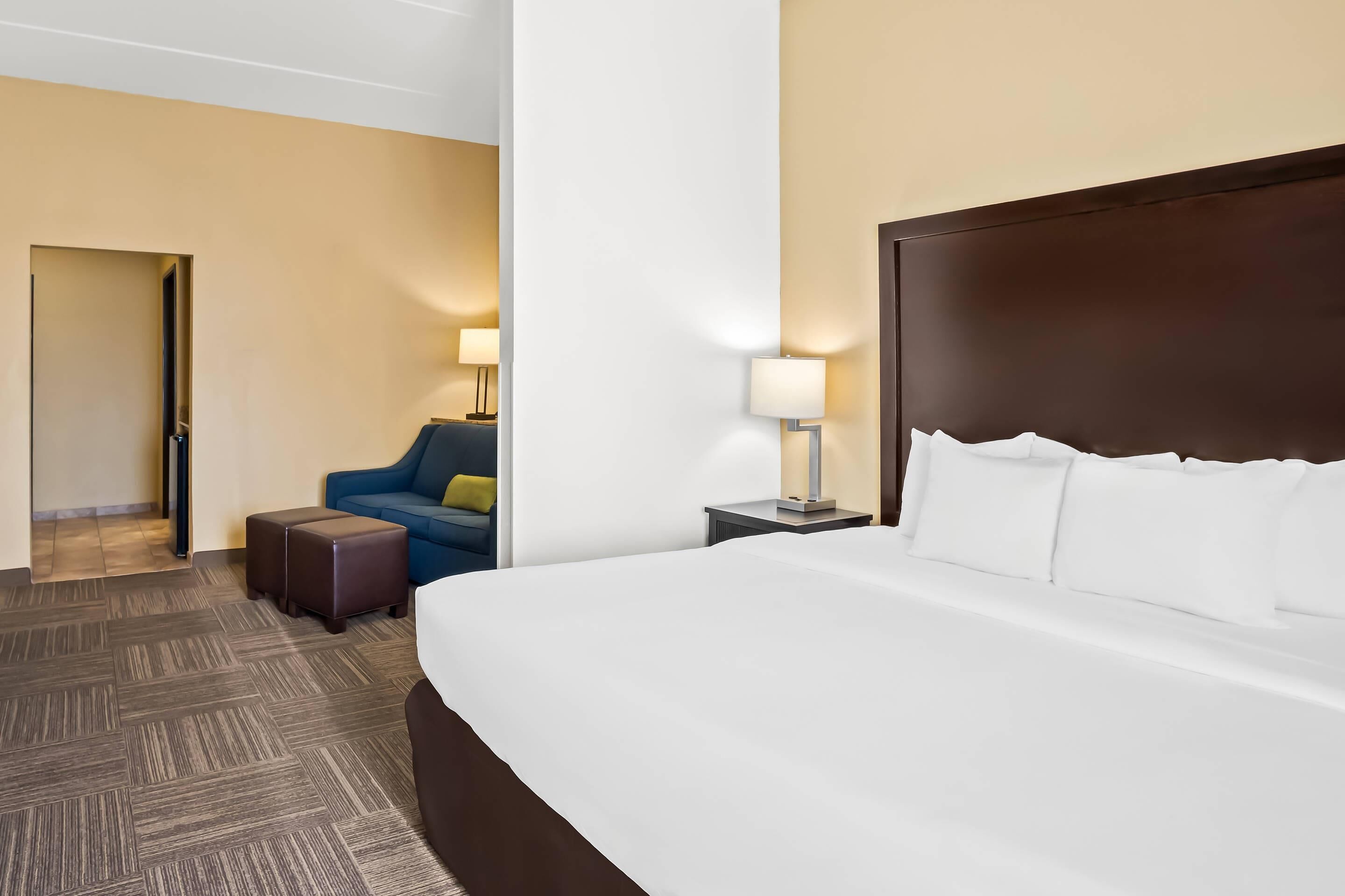 A hotel room with a large bed, a sofa, a nightstand, and a lamp.