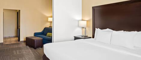 A hotel room with a large bed, a sofa, a nightstand, and a lamp.
