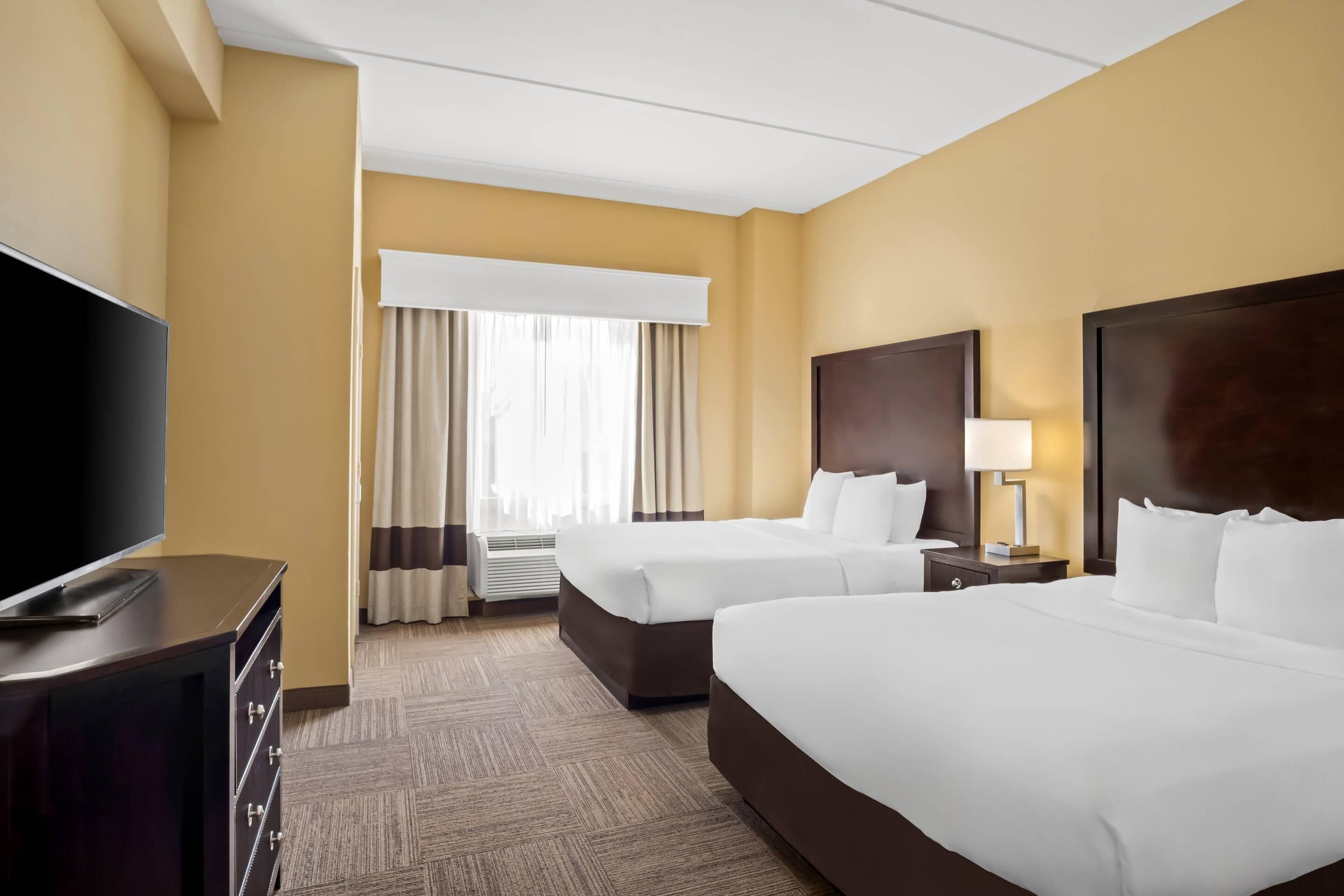 Habitación de hotel con dos camas, televisor de pantalla plana, cómoda y ventana con cortinas.