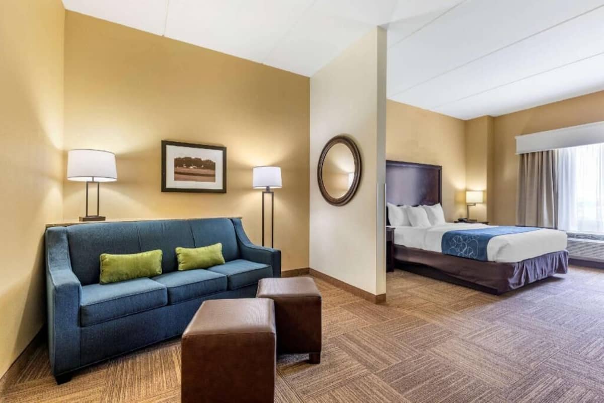 A hotel room with a blue sofa, a bed, a mirror, and a framed picture on the wall.