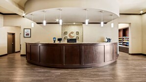 A reception area with a curved dark wood counter, pendant lights, a wall-mounted clock, and a framed picture. - Comfort Suites Frisco (Frisco)