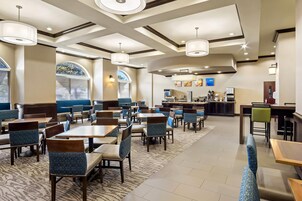 Un comedor de hotel con mesas y sillas, un bar y vistas al exterior a través de grandes ventanales.