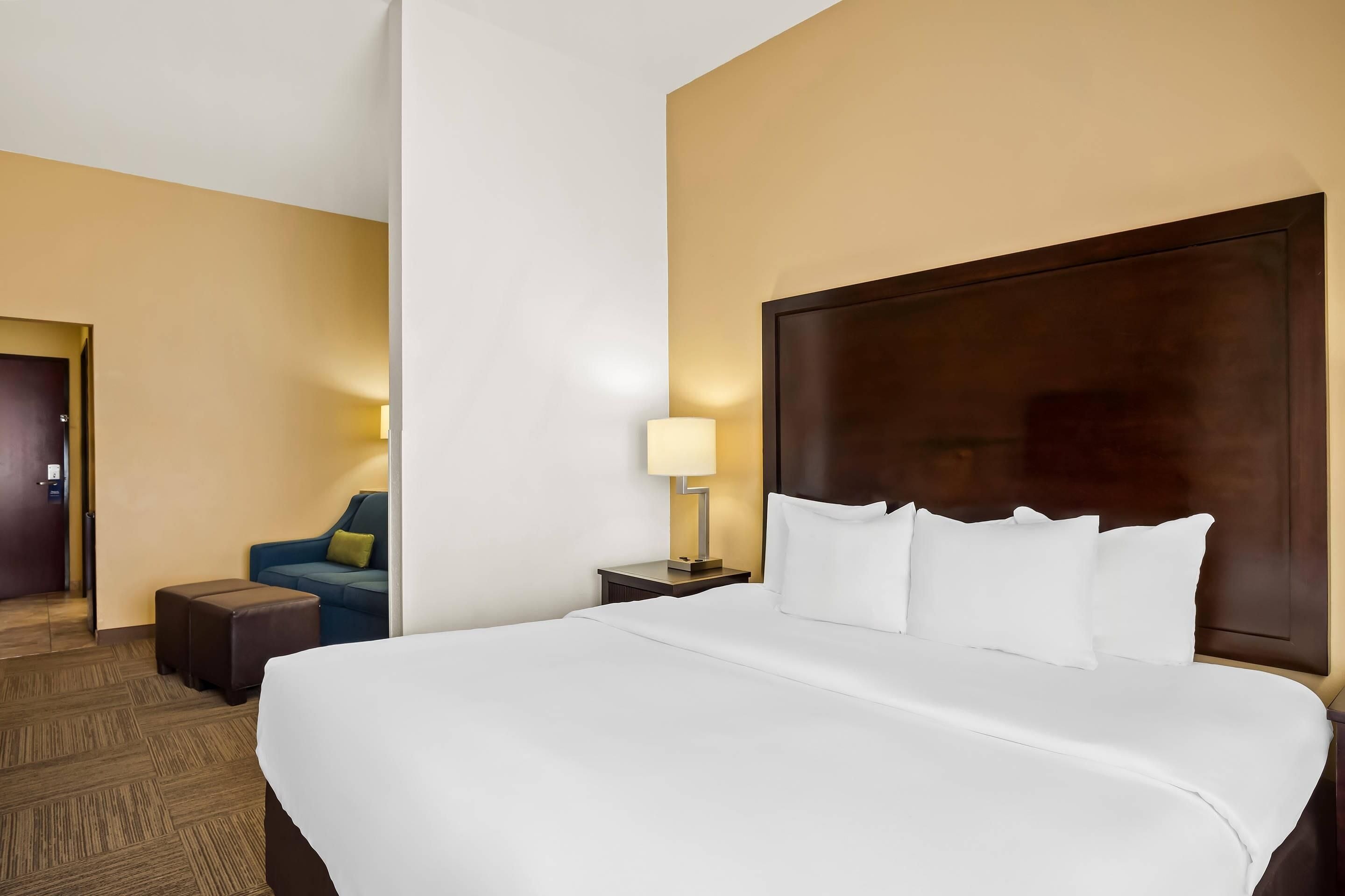 A hotel room with a large bed, a nightstand with a lamp, a blue sofa, and a wooden floor.