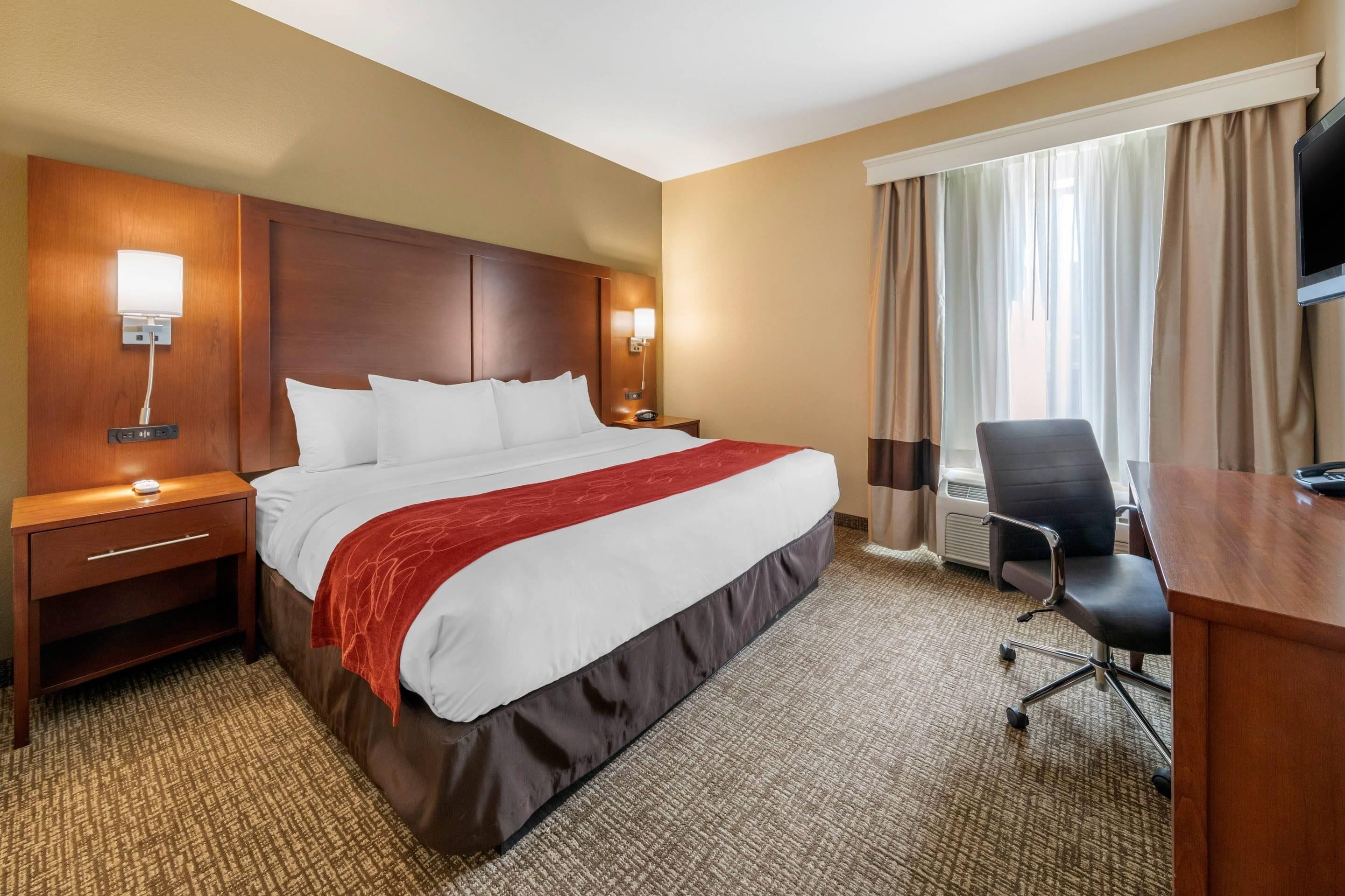 A hotel room with a large bed, a desk, a chair, a TV, and a window with curtains.