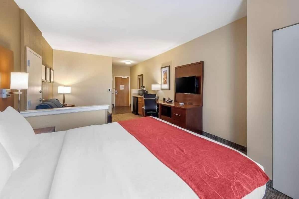Ein Hotelzimmer mit Bett, Schreibtisch, Stuhl, Fernseher und Spiegel.