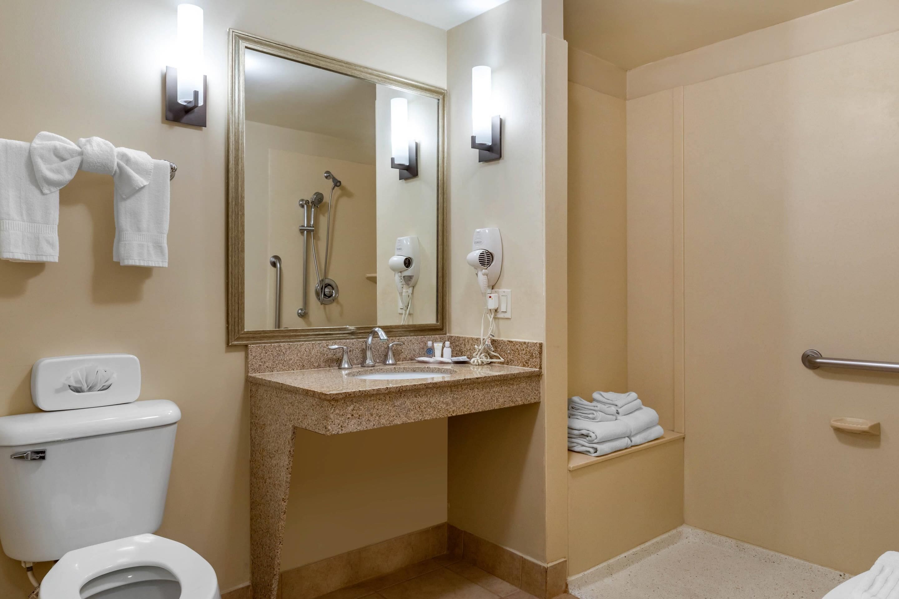 A bathroom with a toilet, sink, mirror, towel rack, and shower.