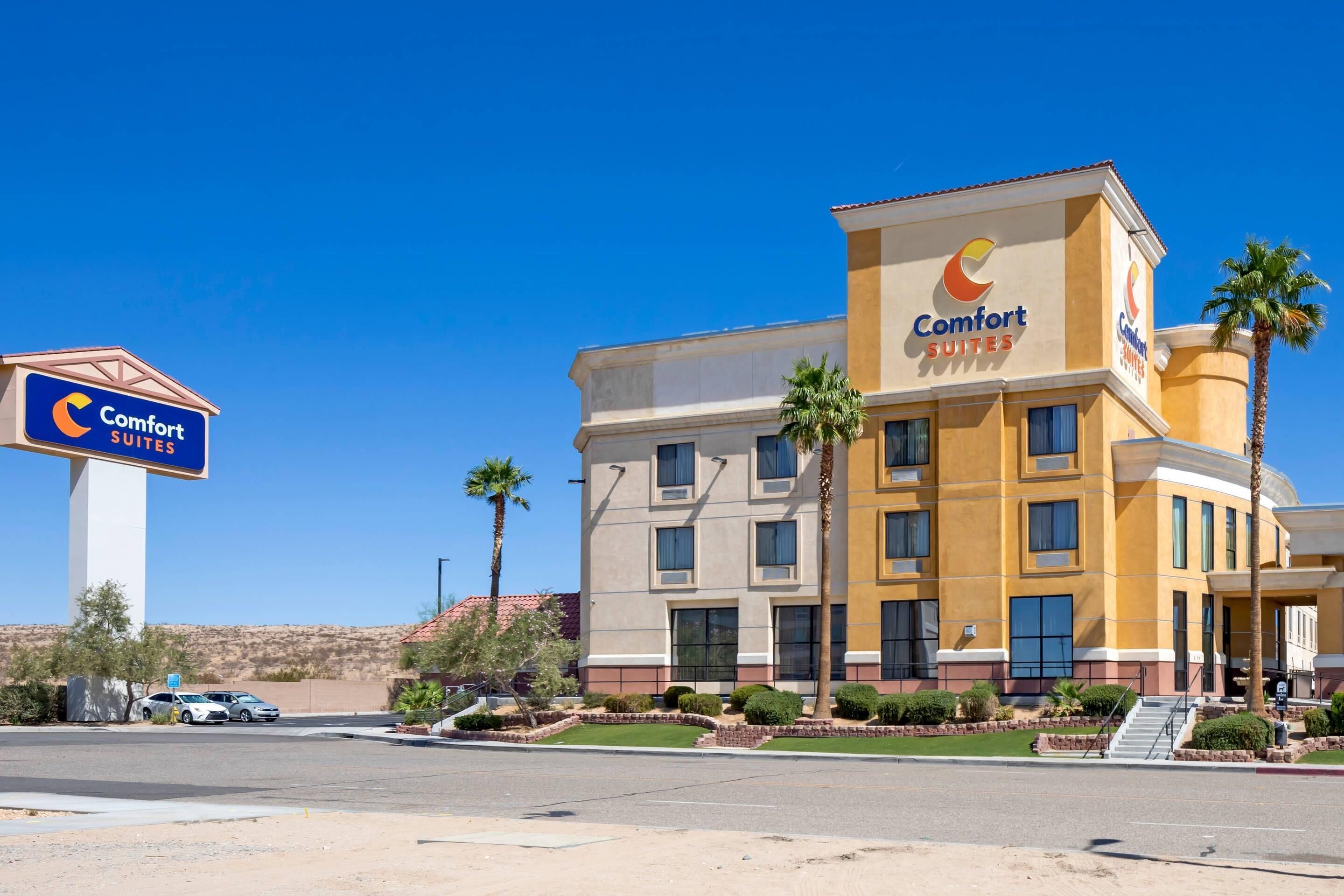 A Comfort Suites hotel with a clear blue sky, palm trees, and a desert landscape.