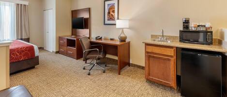 Una habitación de hotel con cama, escritorio, silla, kitchenette y televisor.