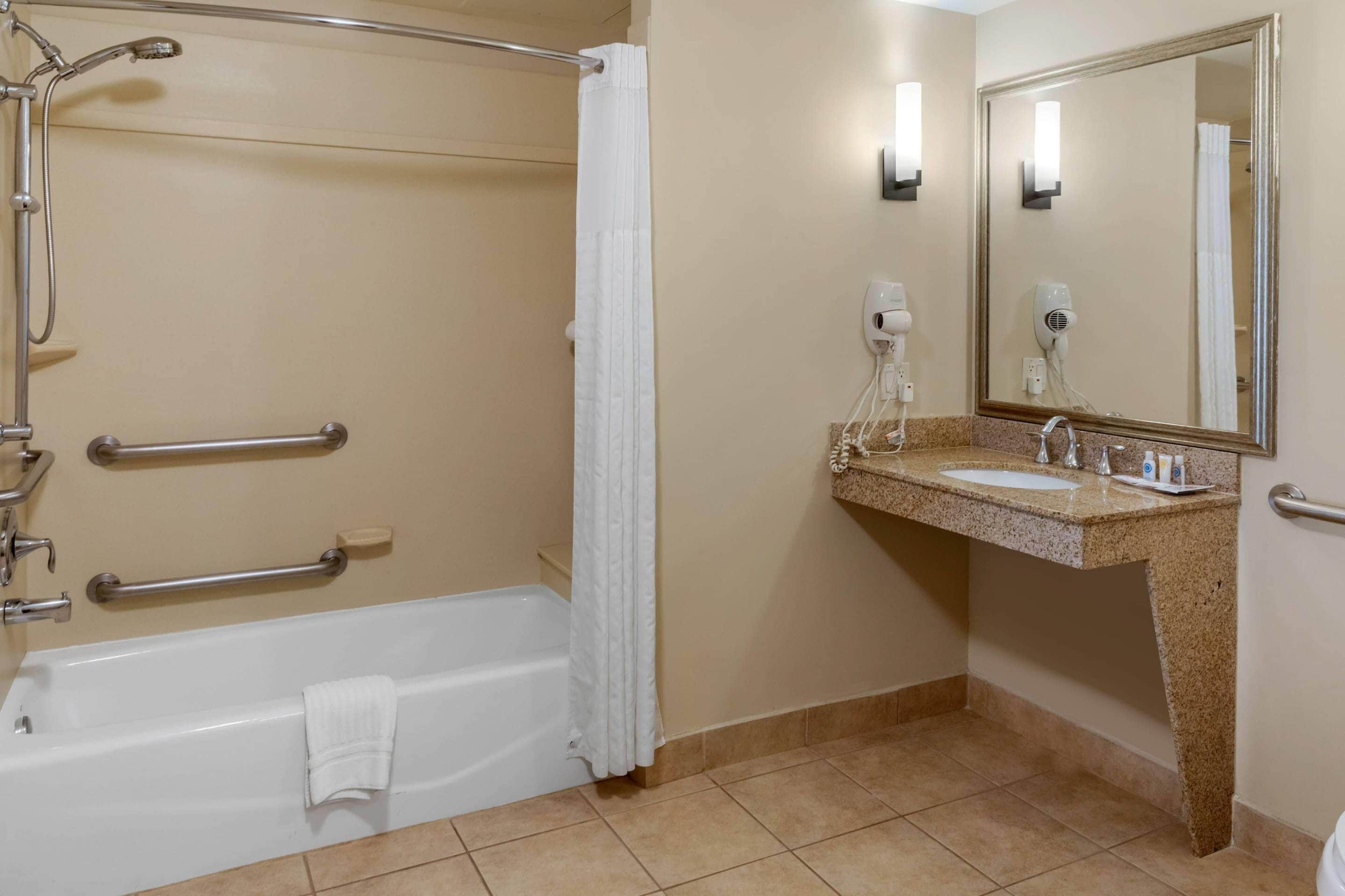 A bathroom with a bathtub, shower, grab bars, a sink, and a mirror.