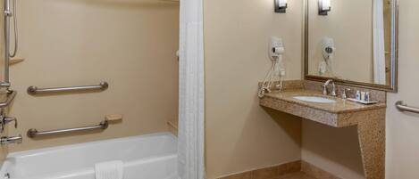 A bathroom with a bathtub, shower, grab bars, a sink, and a mirror.
