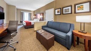 Une chambre d’hôtel avec un lit, un canapé bleu, un pouf marron, un bureau avec une chaise et un téléviseur.
