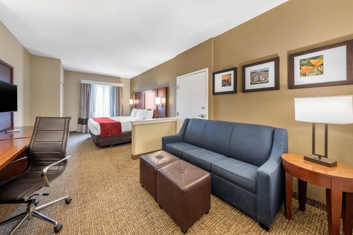 Ein Hotelzimmer mit einem Bett, einem blauen Sofa, einem braunen Hocker, einem Schreibtisch mit Stuhl und einem Fernseher.