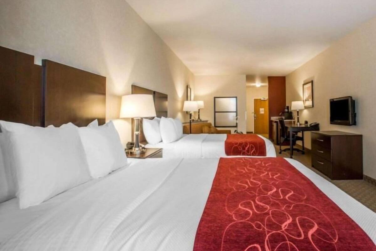 Une chambre d’hôtel avec deux lits, un bureau, une chaise, une télévision et une porte donnant sur une salle de bain.