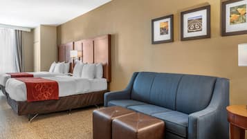 Quarto de hotel com uma cama grande, um sofá azul e um banquinho marrom. Três quadros emoldurados na parede.
