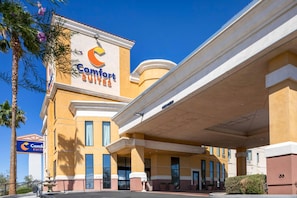 Un hotel con un llamativo letrero de 'Comfort Suites', un acceso cubierto y una palmera.