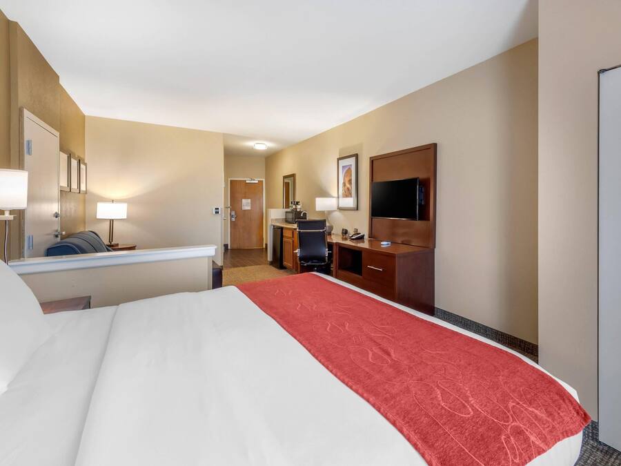 A hotel room with a bed, desk, chair, TV, and a door.