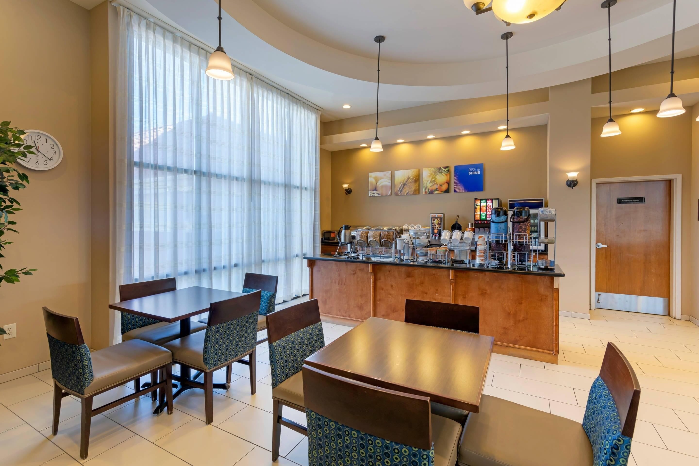 A hotel dining area with a long table, chairs, a bar, and a clock on the wall.