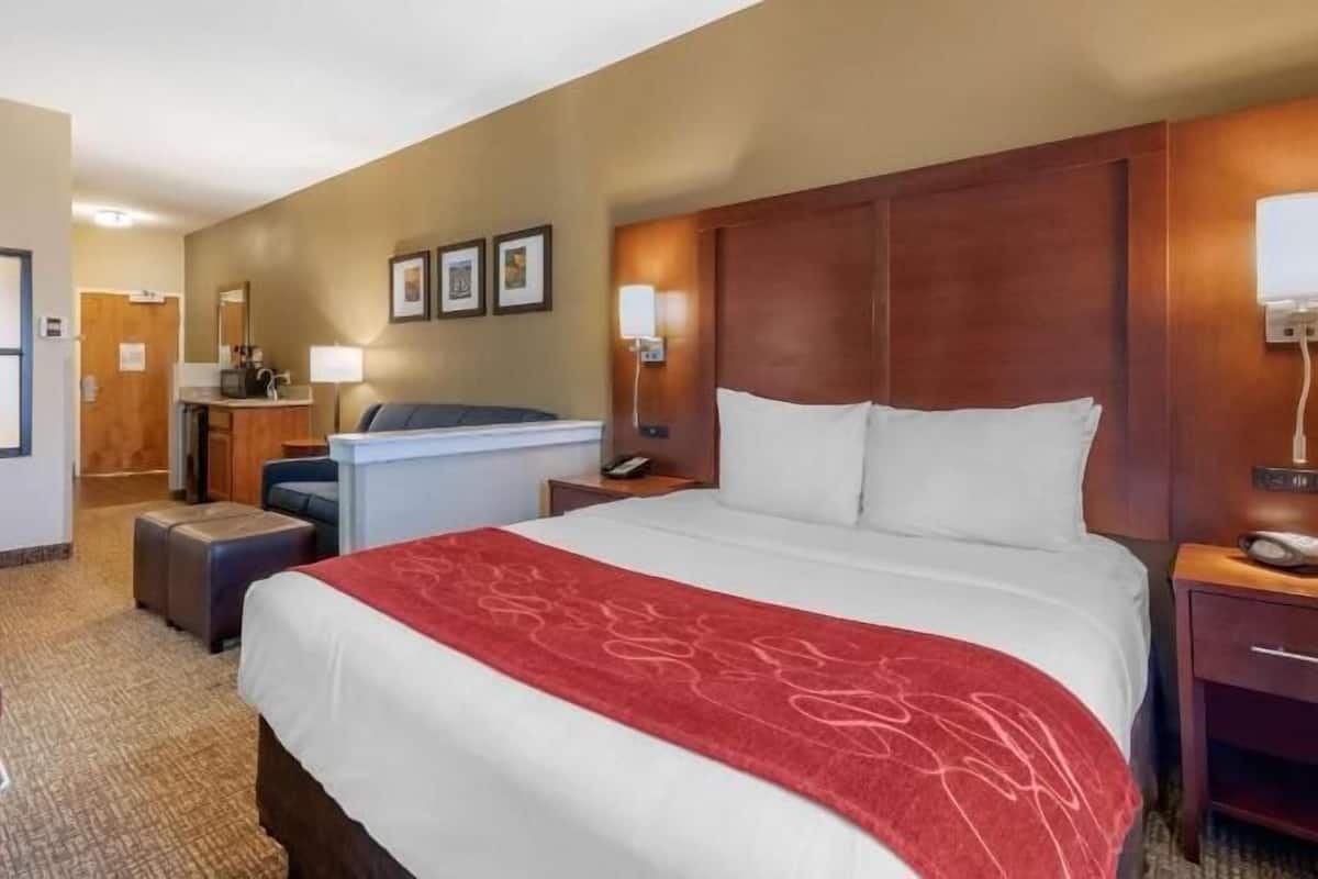 Ein Hotelzimmer mit einem großen Bett, einem Schreibtisch, einem Stuhl, einem kleinen Tisch, einer Lampe und einem Telefon.