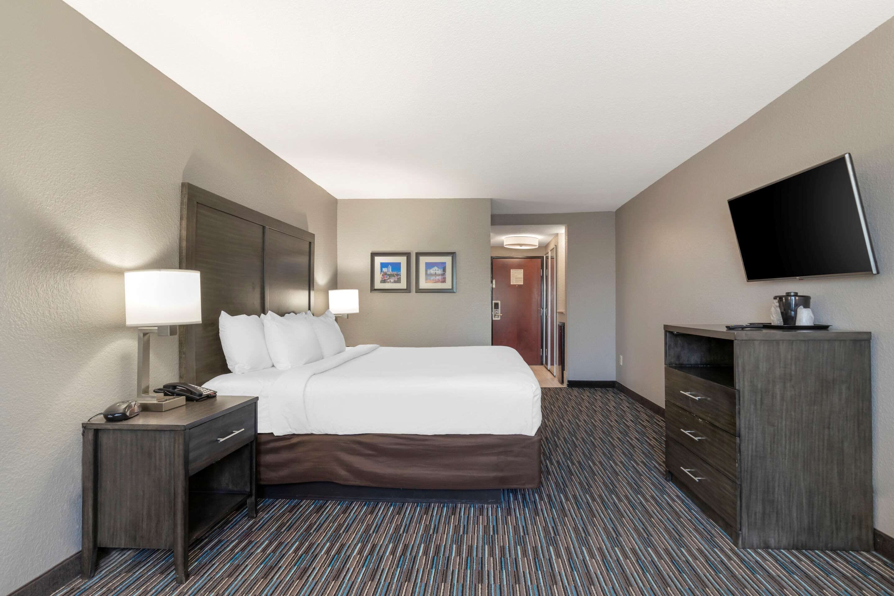Una habitación de hotel con una cama grande, un escritorio con lámpara, televisión y cómoda.