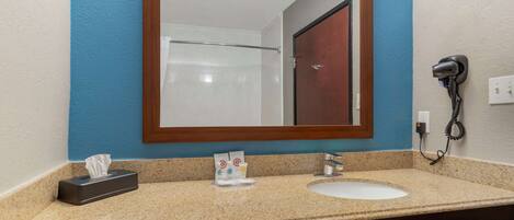 A bathroom with a sink, mirror, towel dispenser, and a hairdryer on the wall.