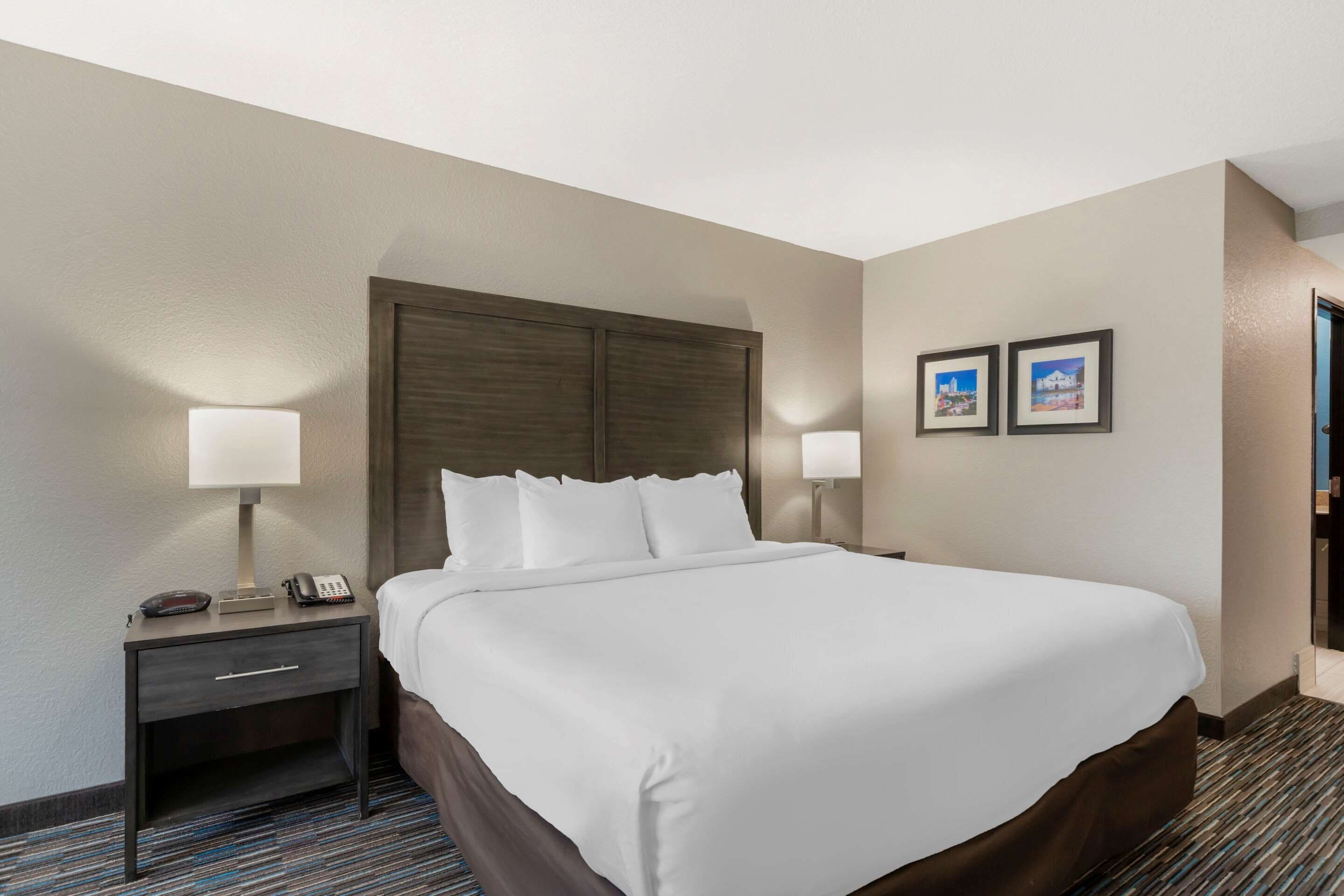 A hotel room with a large bed, two bedside tables, a nightstand, and two wall-mounted lamps.