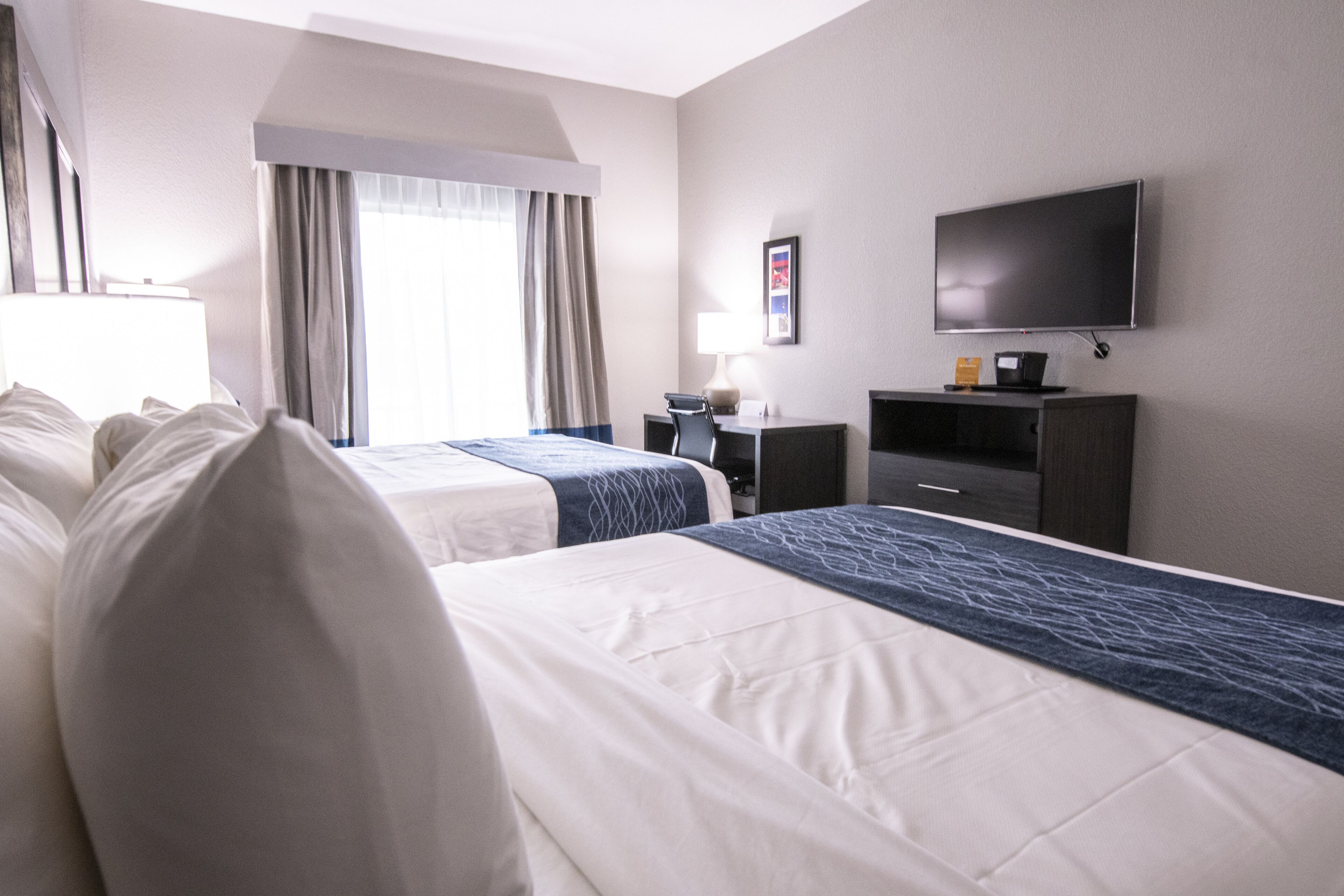 A hotel room with two beds, a desk, a chair, a television, and a window with curtains.