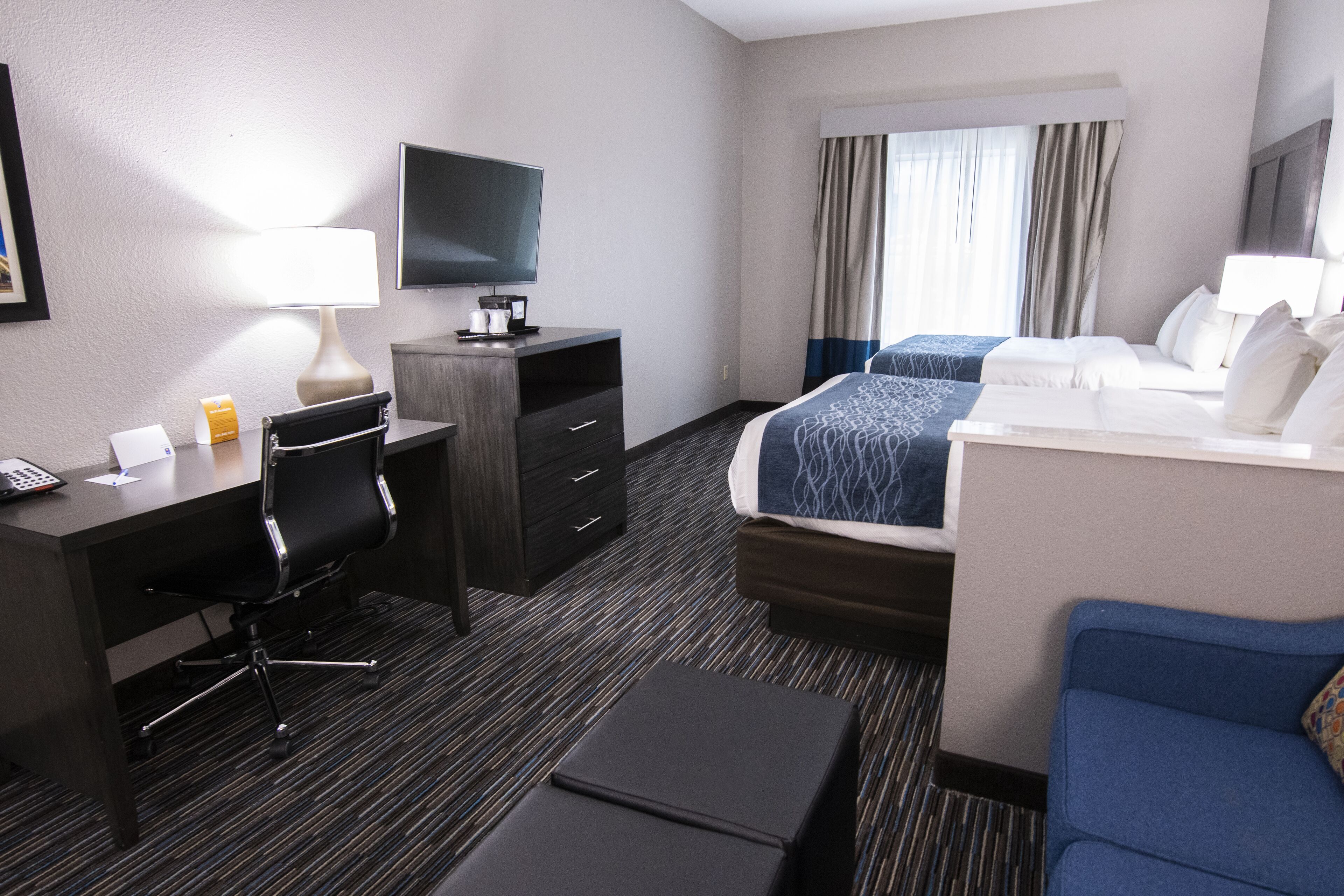 A hotel room with a desk, chair, television, bed, and a blue sofa.
