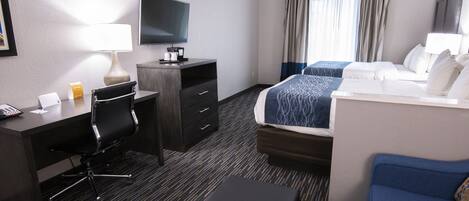 A hotel room with a desk, chair, television, bed, and a blue sofa.