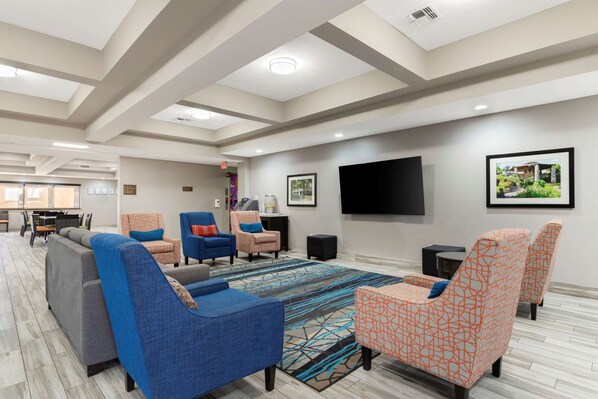 A spacious living area with multiple seating options, a flat-screen TV mounted on the wall, and a patterned rug on the floor.