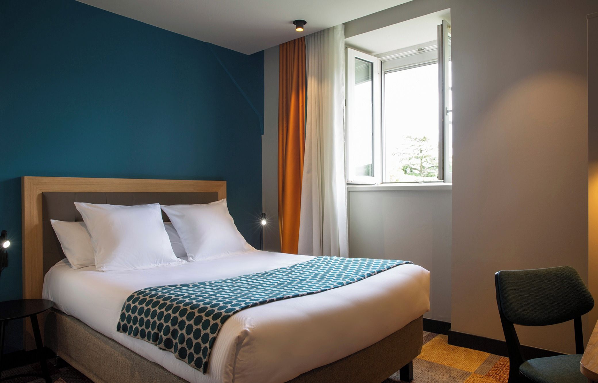 Una camera d'albergo con un letto, una sedia, una finestra e un comodino.