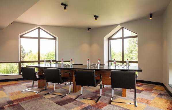 Un salón de conferencias con una larga mesa, cuatro sillas y ventanas amplias.