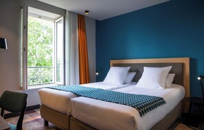 Una habitación de hotel con cama, una silla, ventana con cortinas y vistas a zonas verdes.