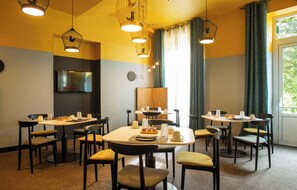 A dining area with multiple tables and chairs, a flat-screen TV mounted on the wall, and a large window with curtains. - The Originals Boutique Htl des Sources Nevers Nord (Pougues-les-Eaux)