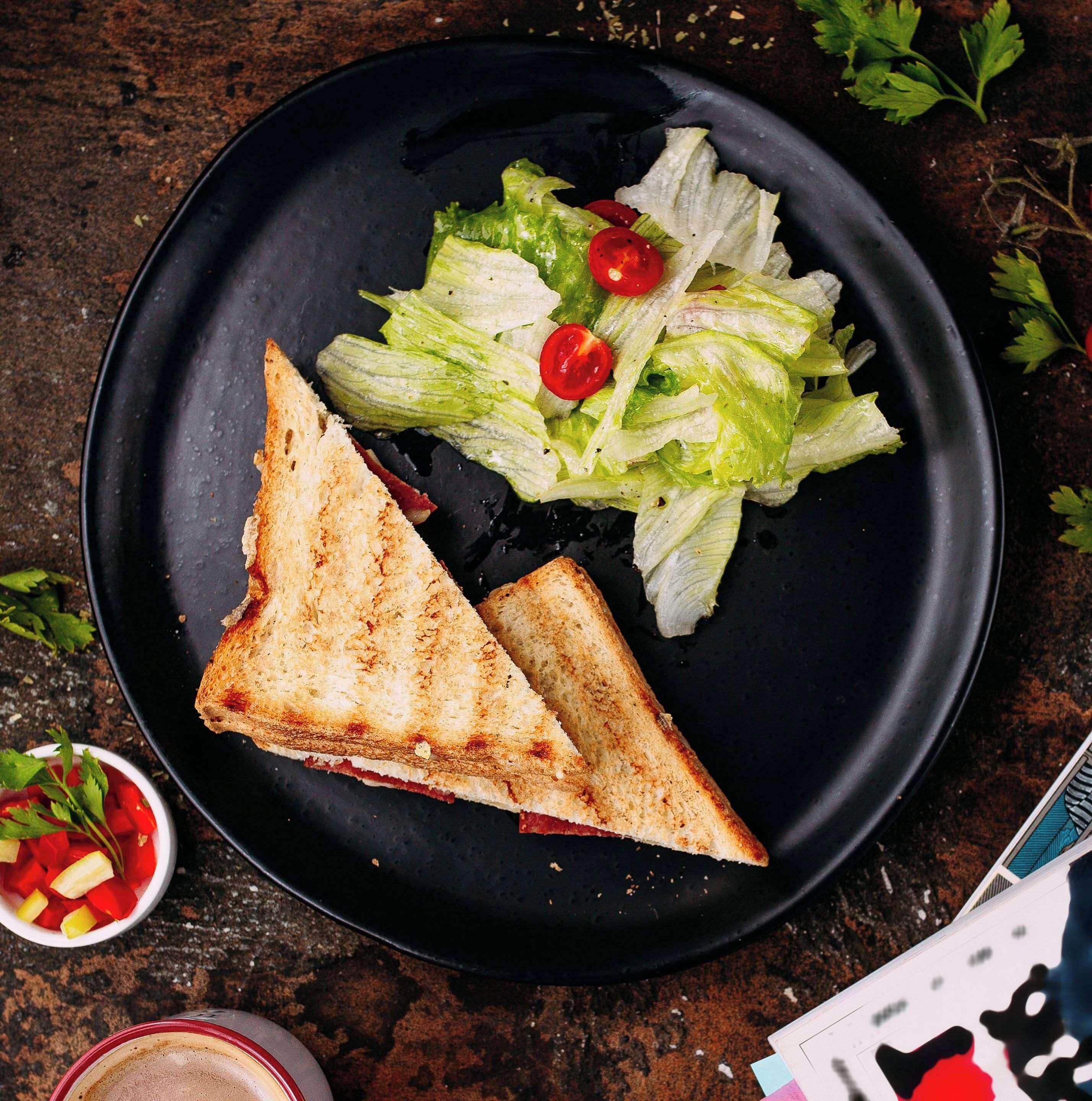 Un plato con pan tostado y una ensalada como acompañamiento sobre una superficie oscura.