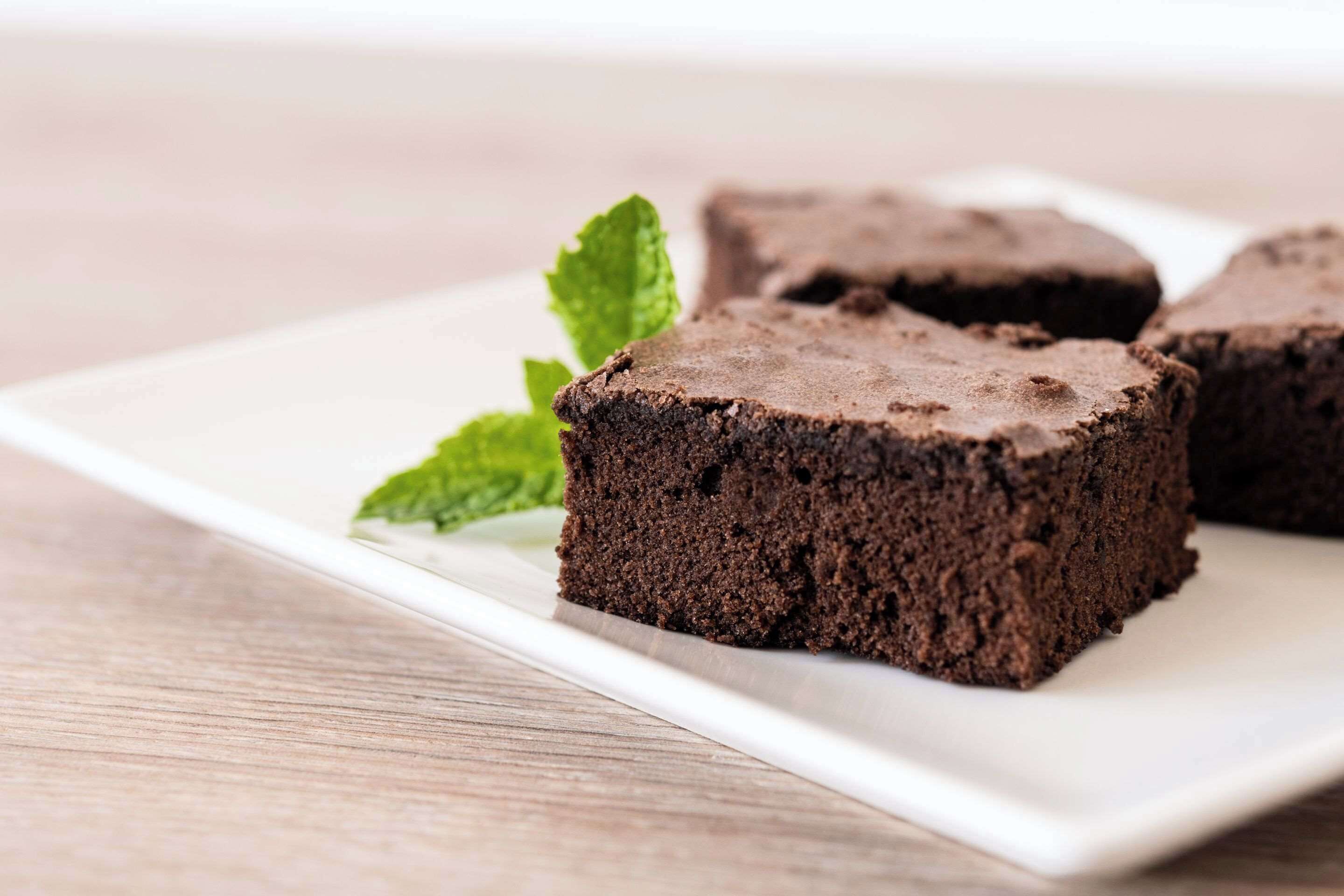 A white plate with three chocolate brownies and a mint leaf.