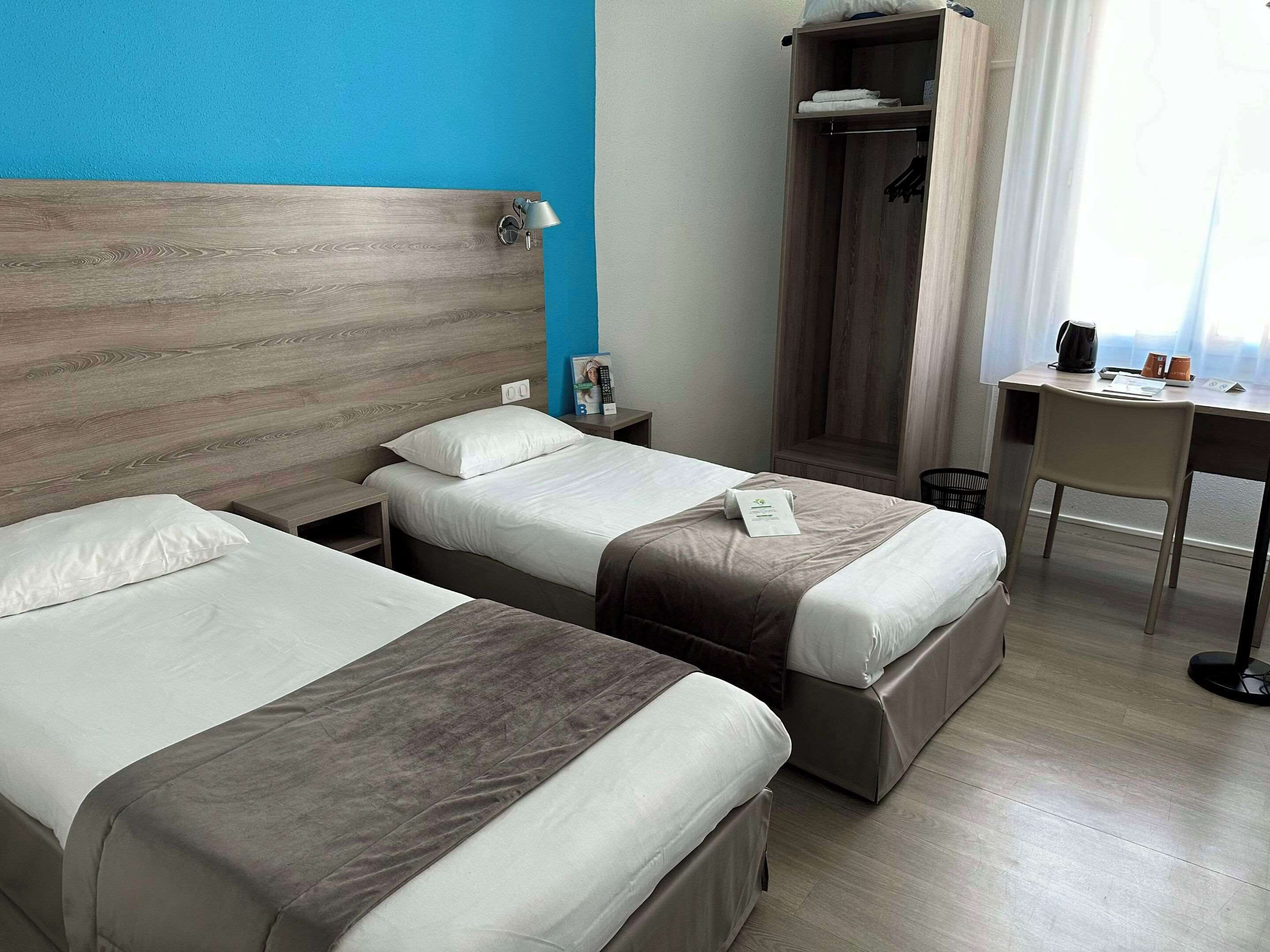 Ein Hotelzimmer mit zwei Betten, einem Schreibtisch, einem Kleiderschrank und einer Duschkabine.