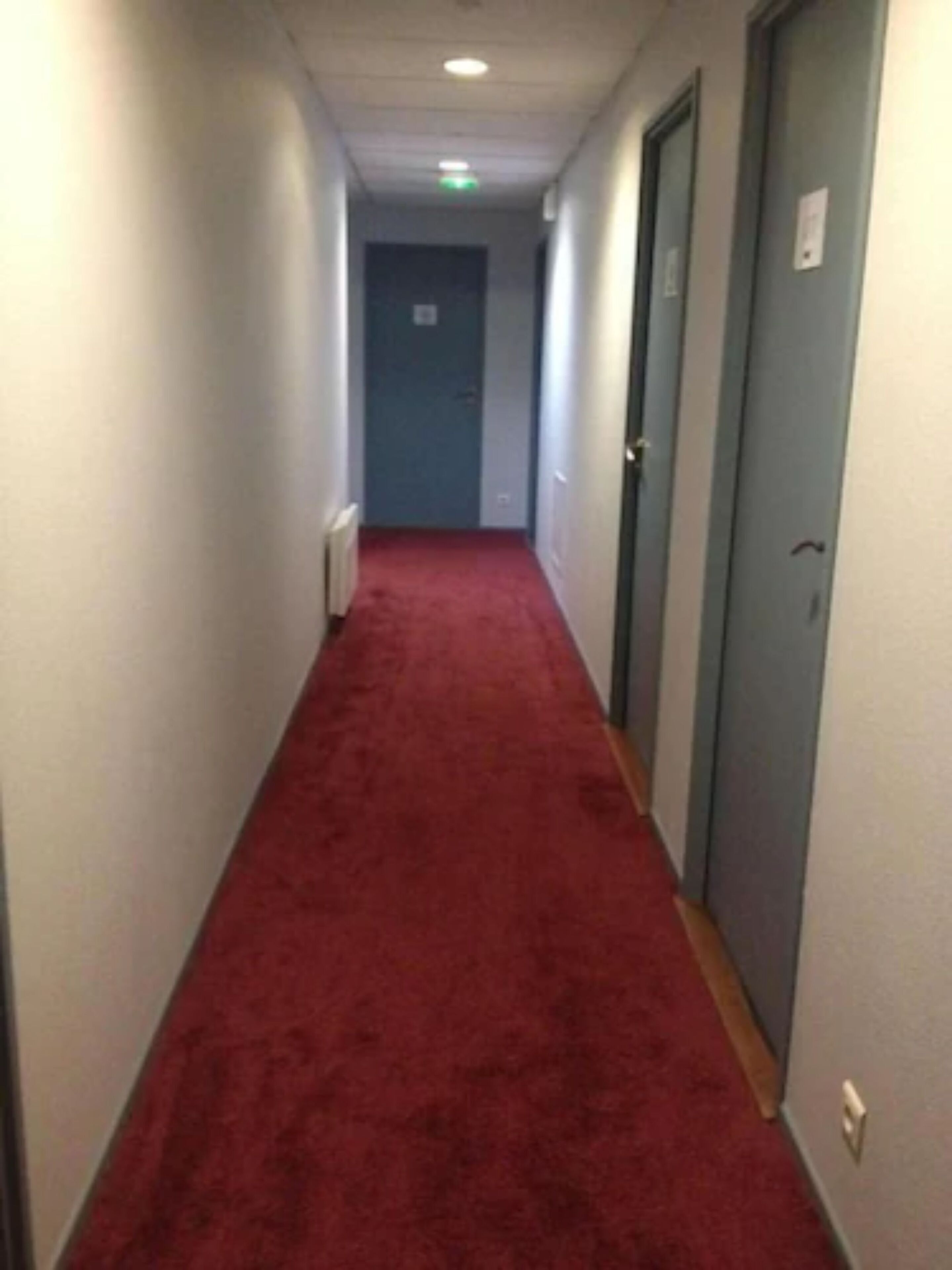 A narrow hallway with a red carpet, white walls, and doors on both sides.