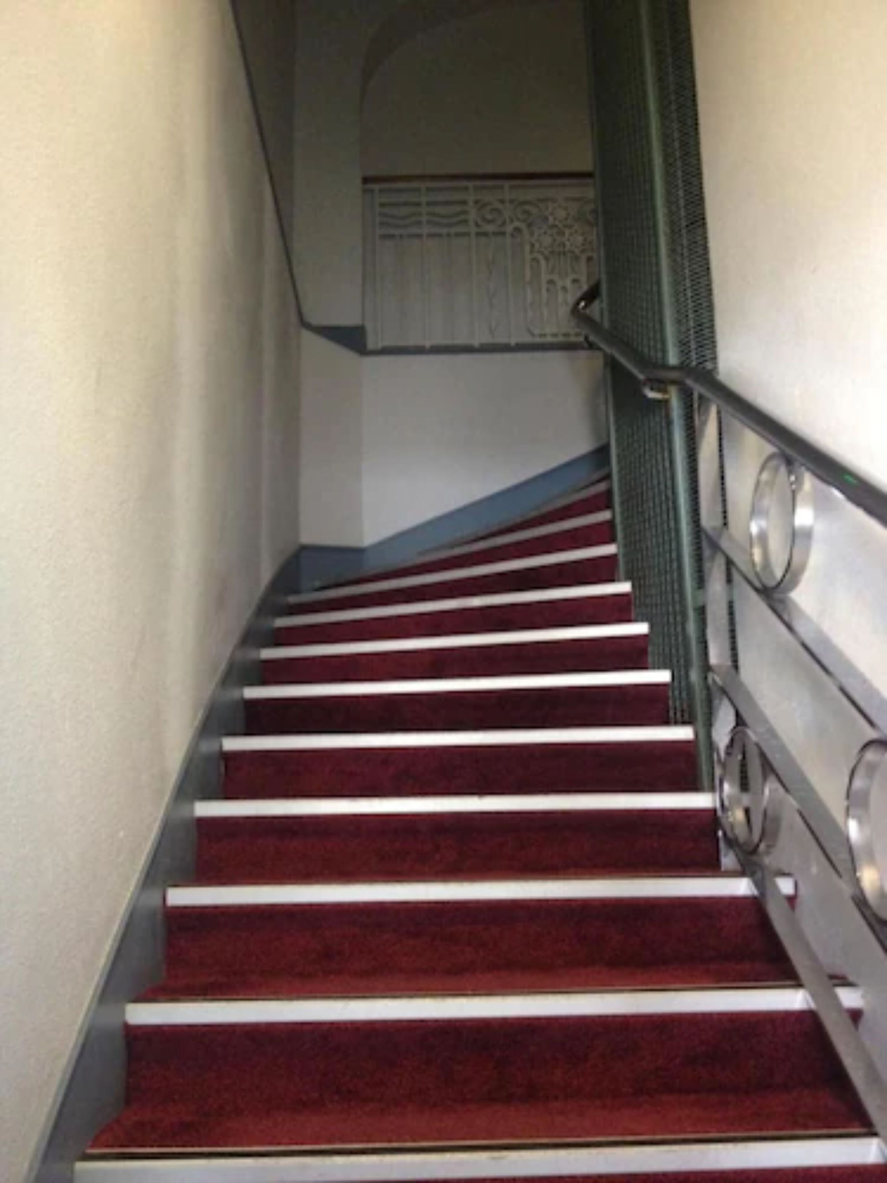 Una escalera con escalones alfombrados de rojo y barandillas metálicas.