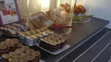 Une table de buffet proposant une variété de plats, notamment des pots de confitures, des plateaux de biscuits et une vitrine remplie de pâtisseries.