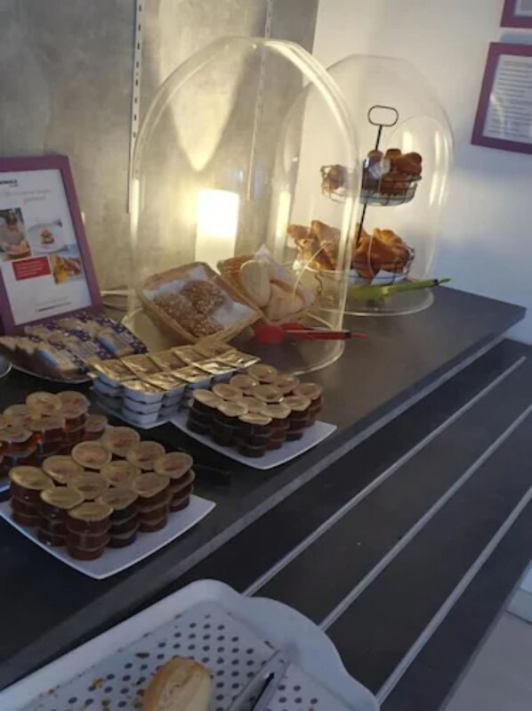 A buffet table with various food items, including jars of preserves, trays of cookies, and a display case with pastries. - BRIT HOTEL CONFORT NEVERS Centre Gare (Nevers)