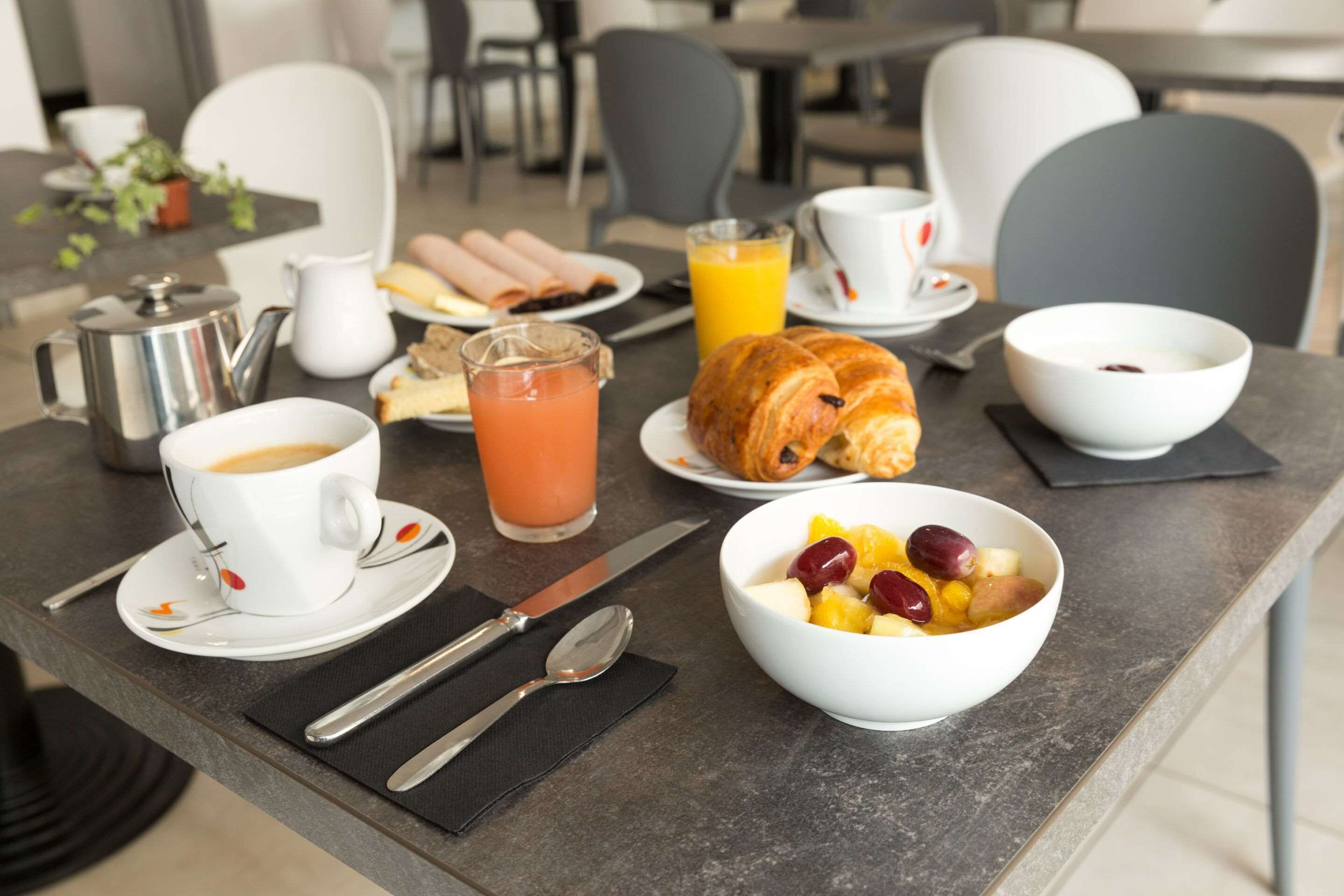 Una mesa de desayuno con cruasanes, fruta, café y jugo.