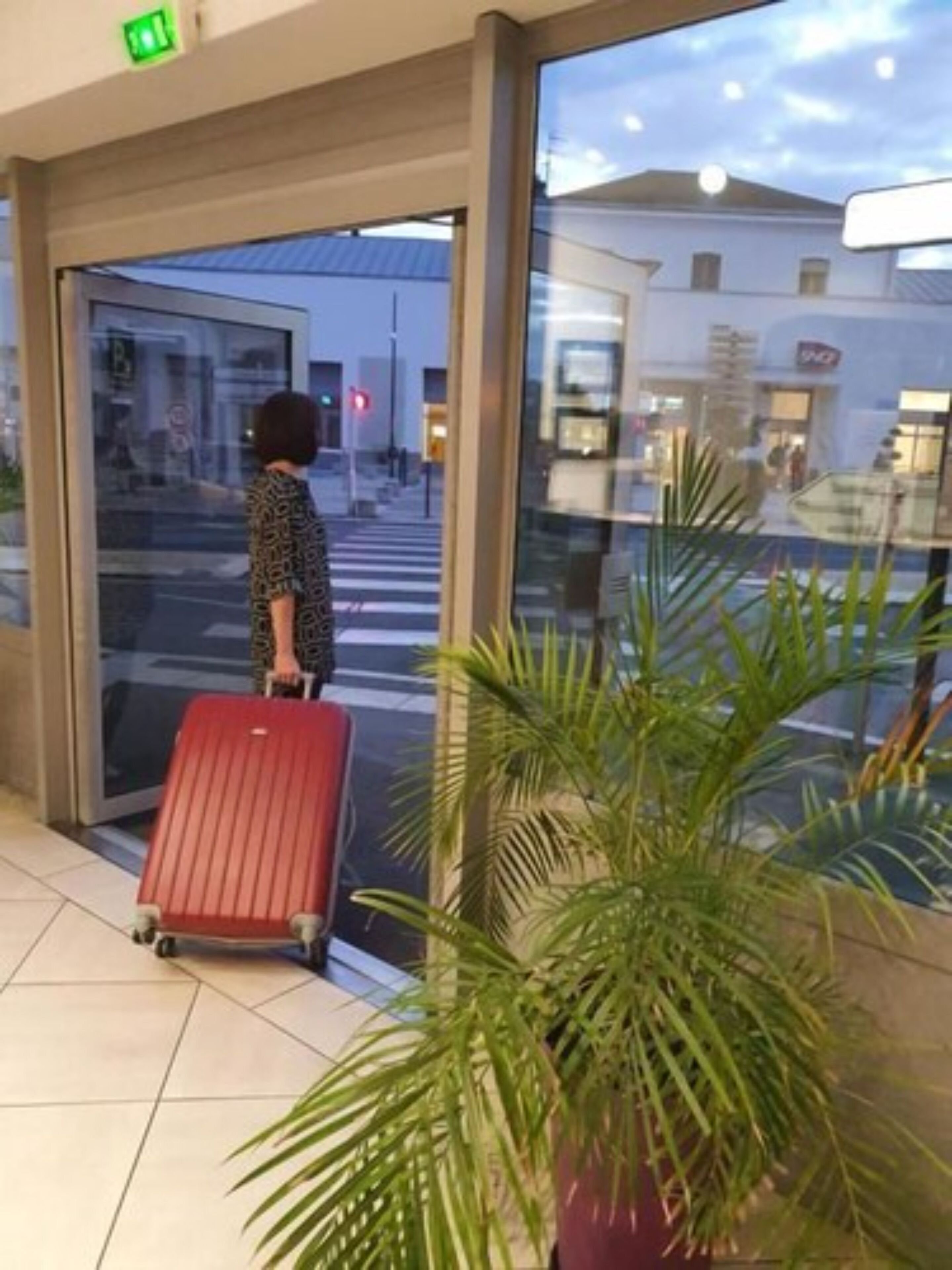 A person with a red suitcase at a hotel entrance.