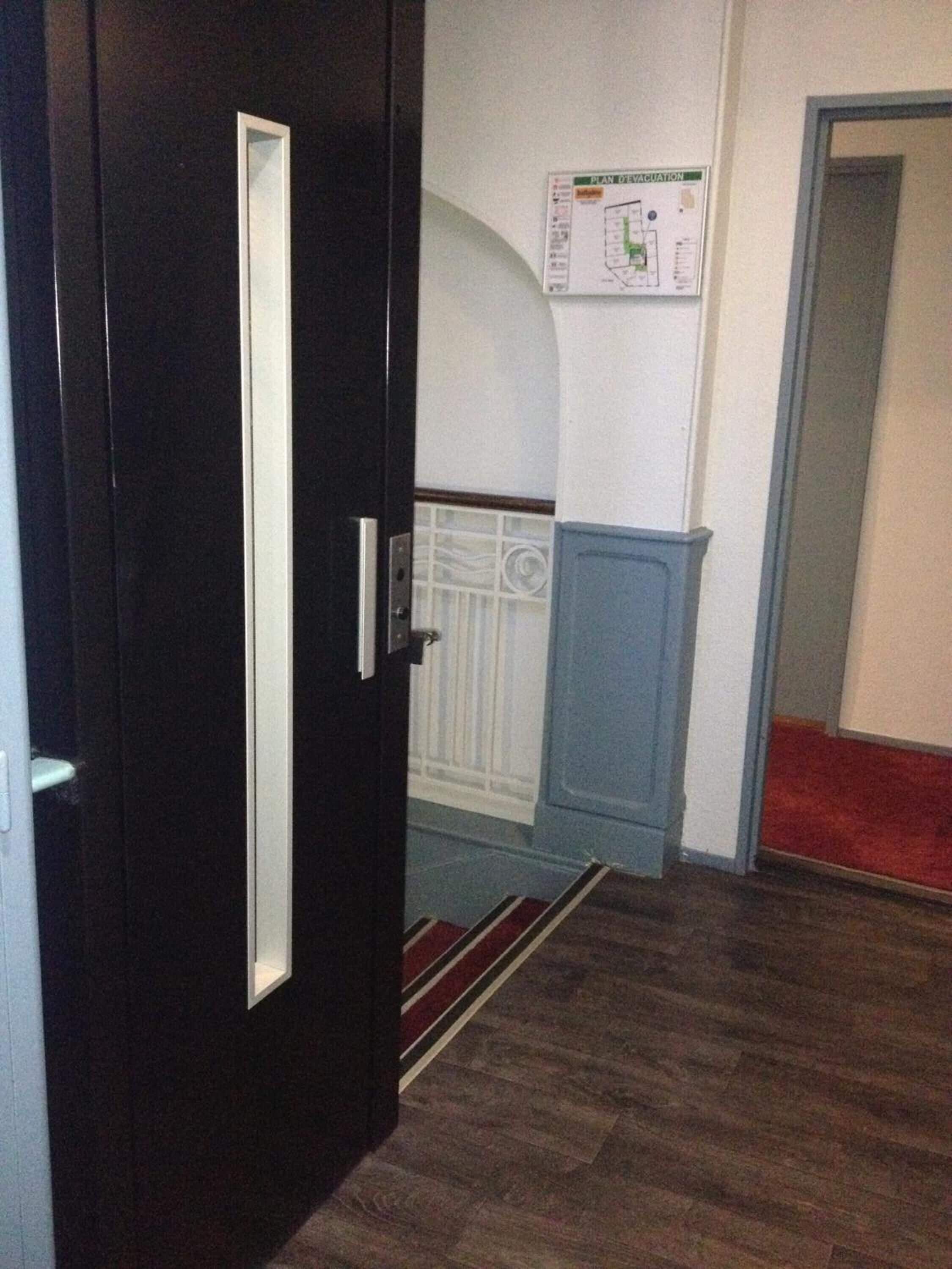 A hallway with a dark wooden door, a blue door frame, a white wall with a map, and a red carpet.