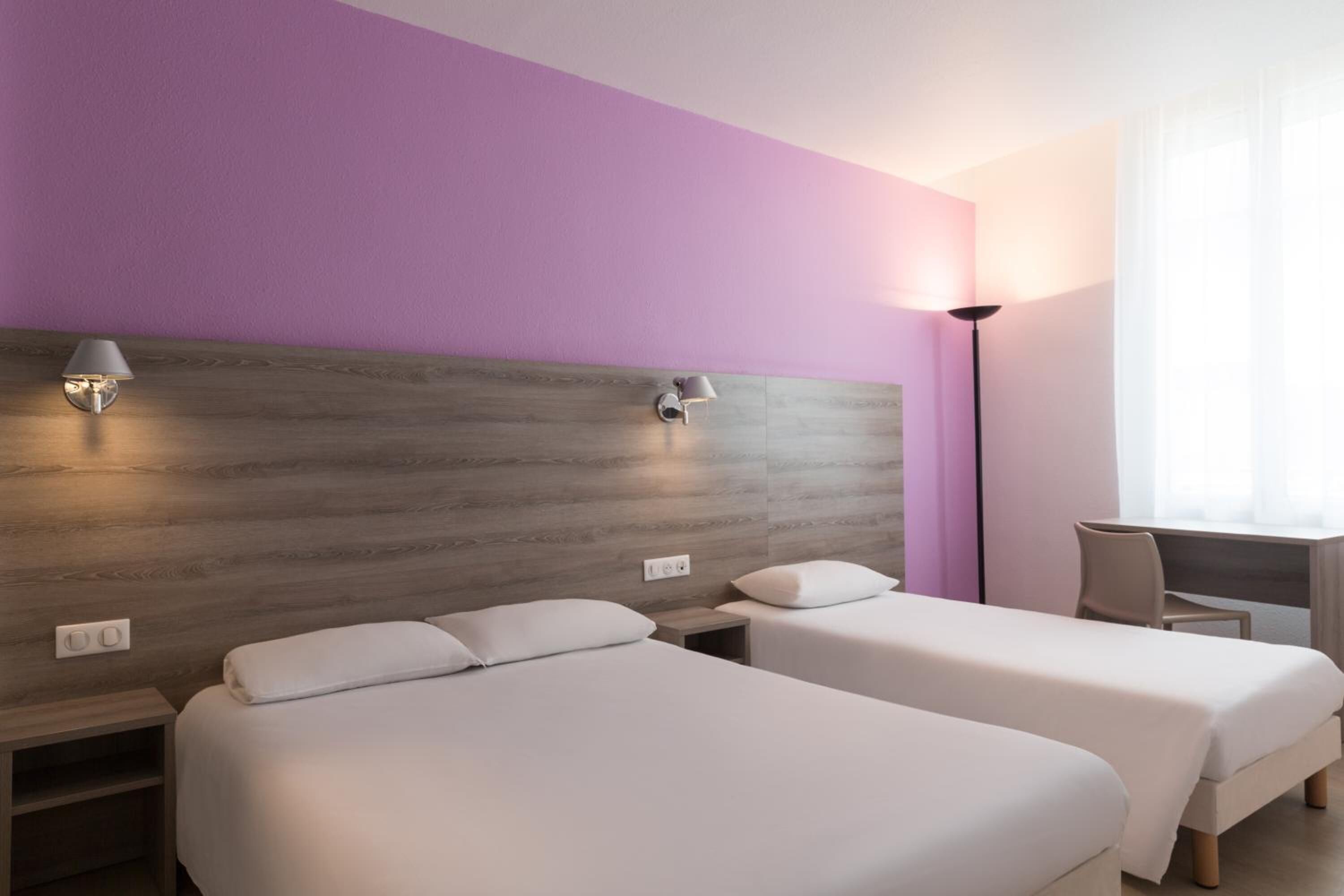 A hotel room with two beds, a desk, and a chair.