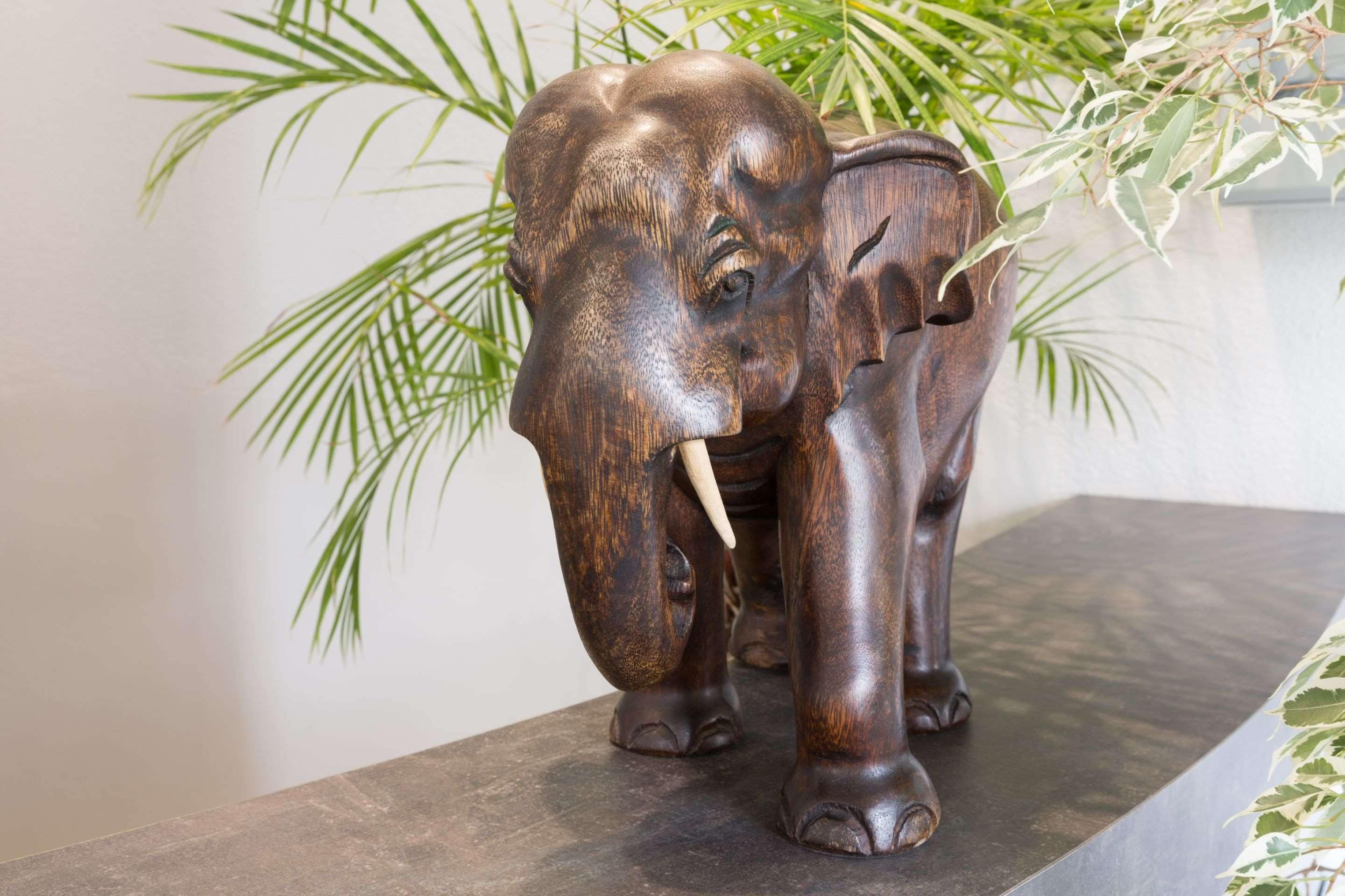 Une sculpture d’éléphant en bois, posée sur une surface en pierre sombre.