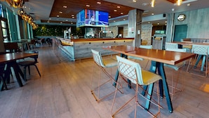 A modern restaurant interior with wooden tables, bar area, and a large TV screen. - Village Hotel Leeds South (Leeds)
