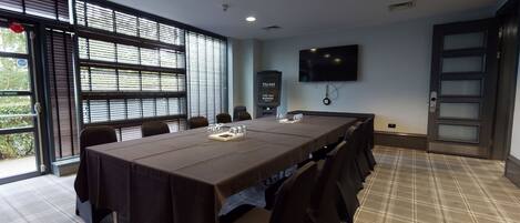 A conference room with a long table, chairs, a TV screen, and a door with frosted glass panels.