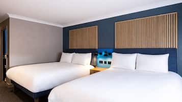 A hotel room with two beds, a wooden headboard, a nightstand, and a wall-mounted light fixture.