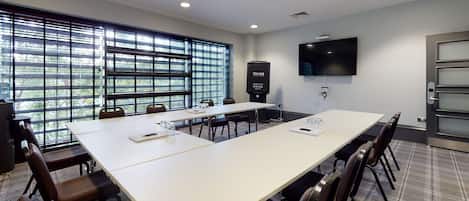 Uma sala de conferências com uma mesa comprida, cadeiras, uma tela de projetor e uma televisão.